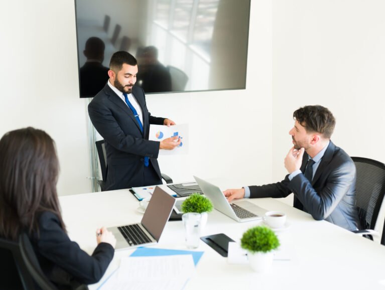Sales are going up in the company. Attractive sales representative showing a graph with the business goals to his co-workers in the meeting room